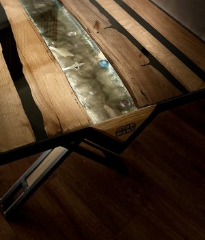 Table Starwars, pieds en métal recouvert de peinture mate, plateau en bois avec rivière époxy transparente. L'intérieur de la rivière est rétro éclairé par batterie qui met en évidence des vaisseaux.